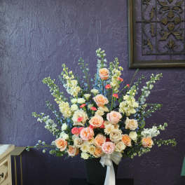 Large peach and cream rose arrangement in a black vase with a white ribbon