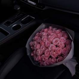 Bouquet of pink roses wrapped in white paper on a car seat