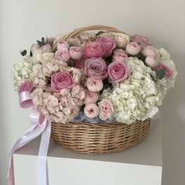 Pink roses and pale hydrangeas in a wicker basket with ribbon