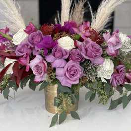 Pink and white roses arranged in a gold vase with tall pampas grass