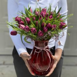 Magenta tulip bouquet in a red glass vase with a pink ribbon