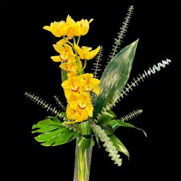 Yellow orchids arranged in a tall glass vase with tropical leaves