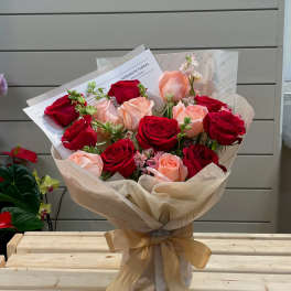 Bouquet of red and blush roses wrapped in cream paper with a gold ribbon