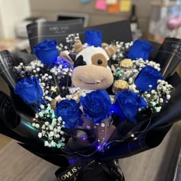 Blue roses arranged around a plush cow with baby’s breath and chocolates