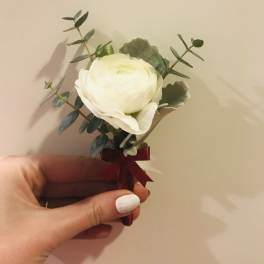 Small white flower boutonniere with greenery and a burgundy ribbon