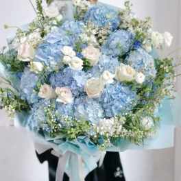Large bouquet of blue hydrangeas and white roses wrapped in pale blue paper