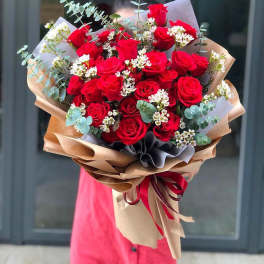 Bouquet of red roses with white filler flowers and eucalyptus in brown paper