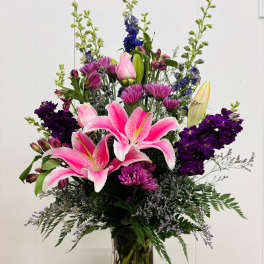 Pink lilies and purple flowers arranged in a clear glass vase