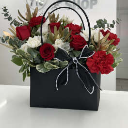 Red and white roses with carnations in a black gift bag