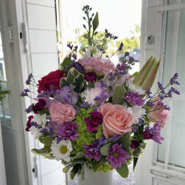 Mixed bouquet of pink, purple, and white flowers in a tall white vase