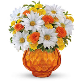 White daisies, yellow mums, and orange roses arranged in a faceted orange glass vase
