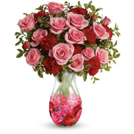 Pink roses and red carnations arranged in a clear glass vase with a rose-print base