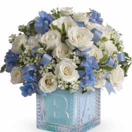 White roses and blue flowers in a glass block vase with a blue ribbon