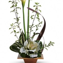 Tall floral arrangement with white calla lilies and greenery in a wooden container