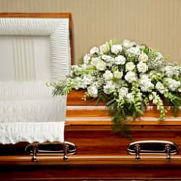 White floral casket spray arranged on a polished wooden casket with white interior.