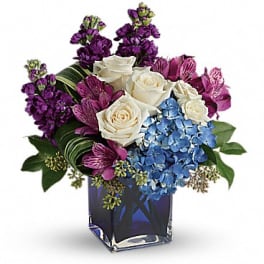 Bouquet of white roses, blue hydrangea, and purple flowers in a glass vase