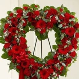 Heart-shaped wreath of red flowers with a red ribbon on a stand