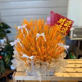 Orange wheat arrangement in a basket with white ribbon bows and a red sign