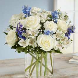White roses and blue flowers arranged in a clear glass vase