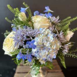 Bouquet of cream roses, blue flowers, and lavender blooms in a glass vase