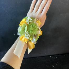 Yellow and green wrist corsage with ribbon ties on a hand