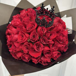 Bouquet of red roses wrapped in dark paper with a black crown topper