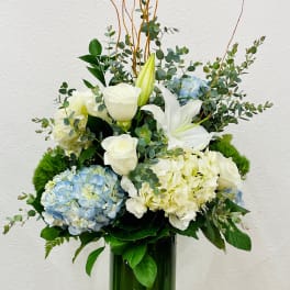 White lilies, roses, and blue hydrangeas in a tall green vase