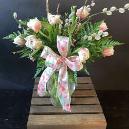 Pink and white tulips in a glass vase with a floral ribbon