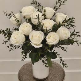 White roses arranged in a white vase with dark greenery