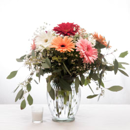 Mixed gerbera bouquet in a glass vase with a small candle