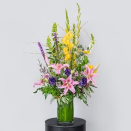 Tall mixed bouquet with pink lilies and purple flowers in a green glass vase