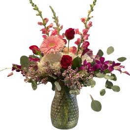 Pink and red mixed flower arrangement in a green glass vase