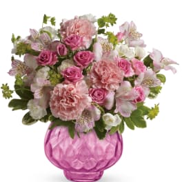 Pink carnations, roses, and white alstroemeria arranged in a round pink glass vase