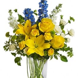 Yellow lilies and roses with blue and white flowers in a clear vase