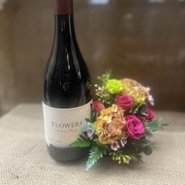 Wine bottle beside a small pink and peach floral arrangement