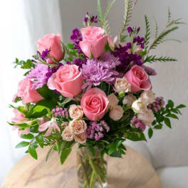 Mixed bouquet of pink roses, lavender mums, and cream spray roses in a clear glass vase