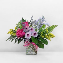 Pink roses and lavender daisies in a clear glass vase with a pink ribbon