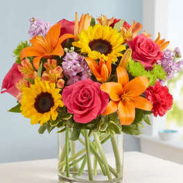 Bright mixed bouquet of sunflowers, roses, lilies, and carnations in a glass vase