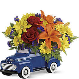 Bouquet of red roses, orange lilies, and yellow daisies in a blue truck container