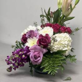 Mixed bouquet of roses, lilies, hydrangea, and purple flowers in a low vase