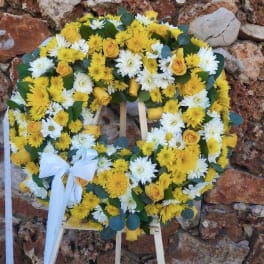 Yellow and white floral wreath on a stand with a white ribbon