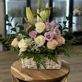 Basket arrangement of roses and lilies in soft pink, cream, and lavender