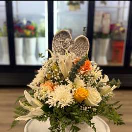 White and peach floral basket with roses, lilies, and an angel figurine.