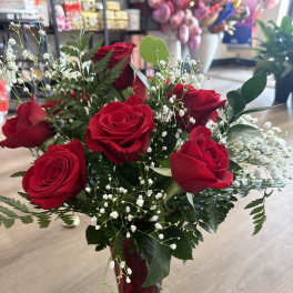 Red roses arranged in a red glass vase with white baby's breath.