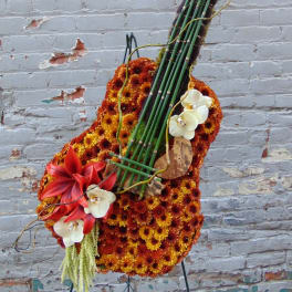Tall floral arrangement shaped like a guitar with orange mums, red lilies, and white orchids on an easel.