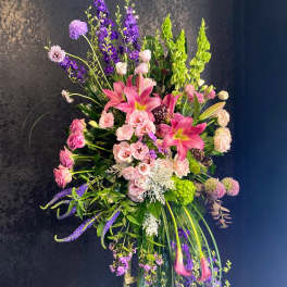 Tall standing spray of pink lilies and mixed purple flowers on a wooden easel.