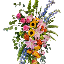 Tall standing floral spray with pink lilies, roses, sunflowers, and blue delphinium
