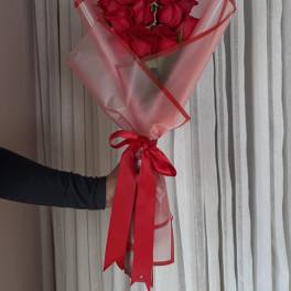 Handheld bouquet of red roses wrapped in frosted cellophane with a red ribbon bow.