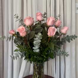 Pink roses arranged in a clear glass vase with eucalyptus foliage