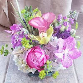 Mixed bouquet with pink calla lilies, orchids, and a peony in a low container